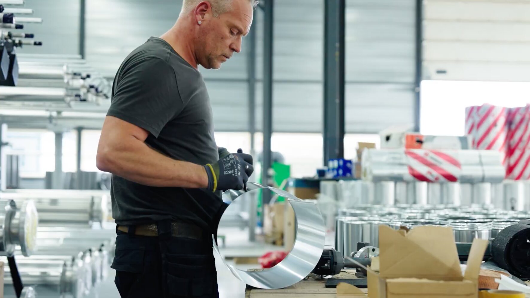Medewerker buigt een aluminium mantel rond tussen voorraad isolatiemateriaal in de werkplaats