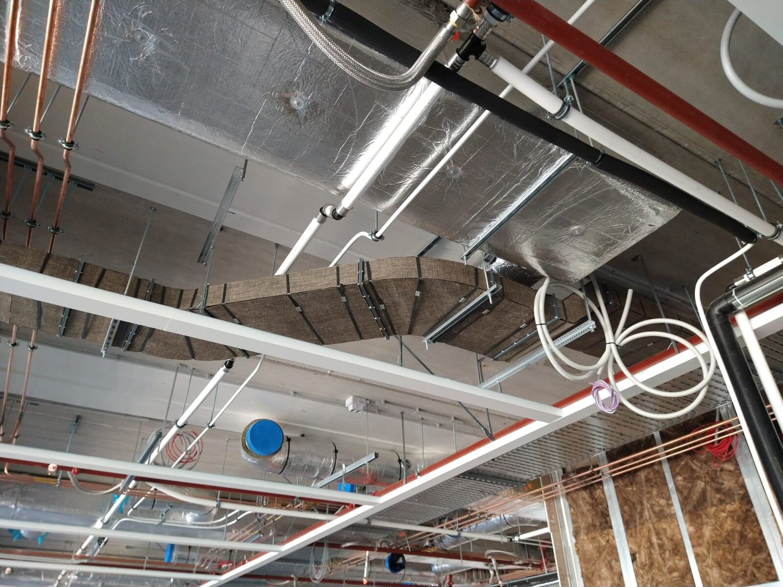 Luchtkanalen met steenwolisolatie en aluminiumfolie tussen leidingen en kabelgoten onder een plafond