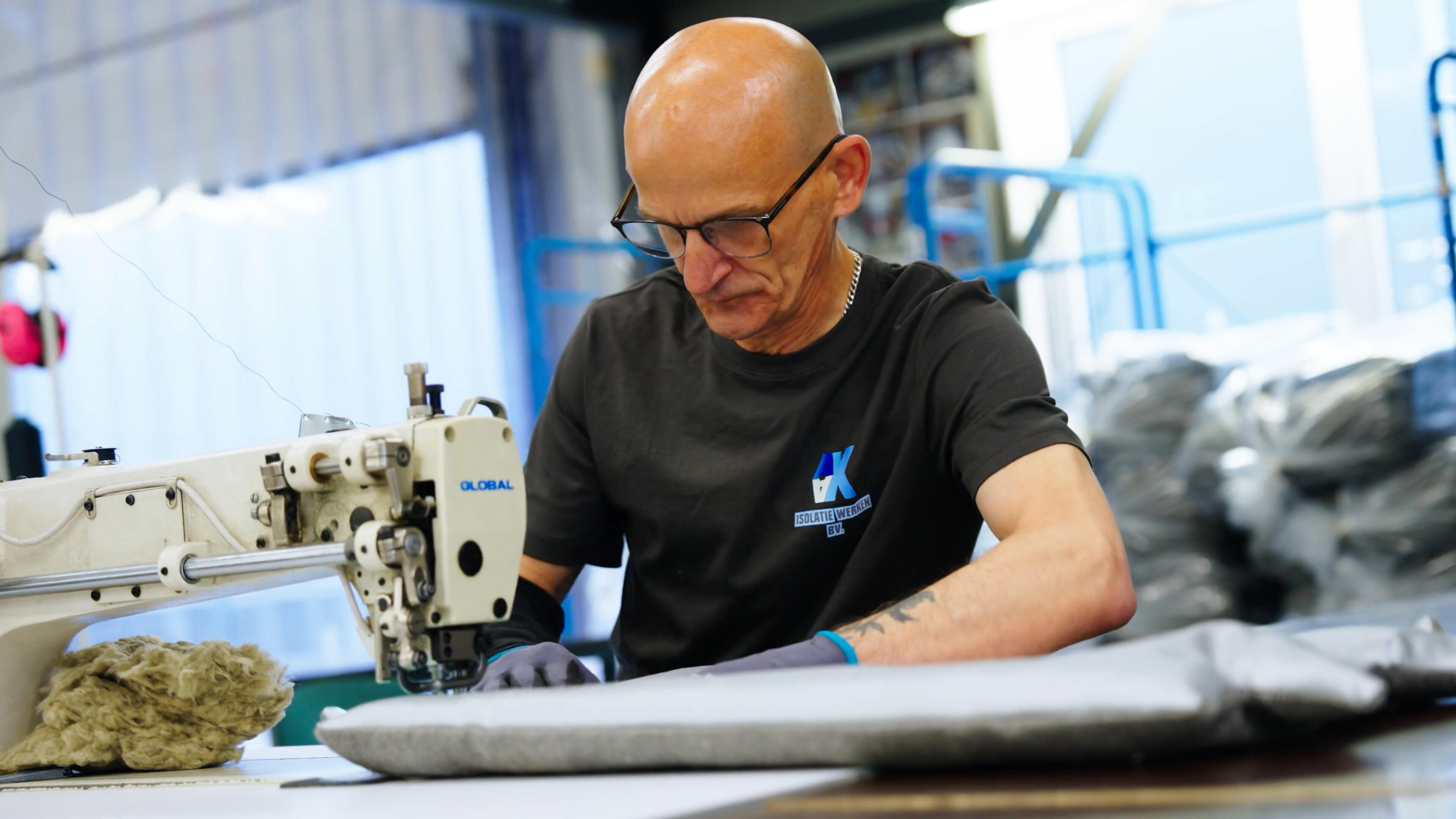 Medewerker van AX Isolatiewerken naait een isolatiematras op een industriële naaimachine