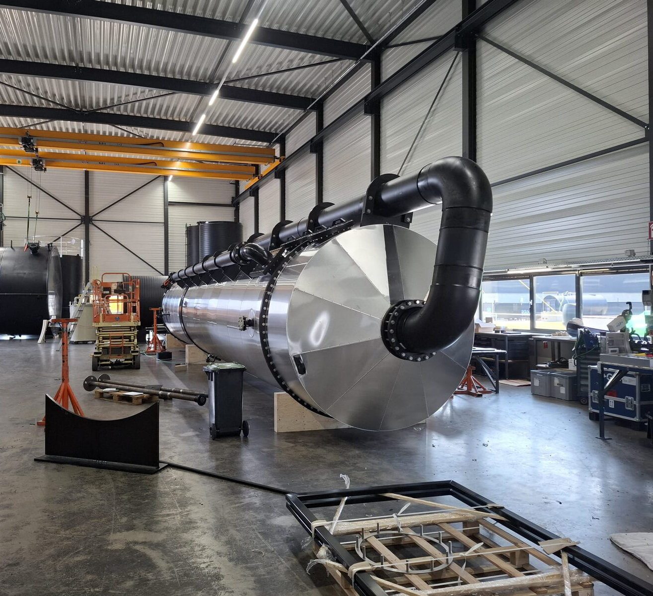 Grote liggende tank met aluminium ommanteling en zwarte leidingbocht in een werkplaats