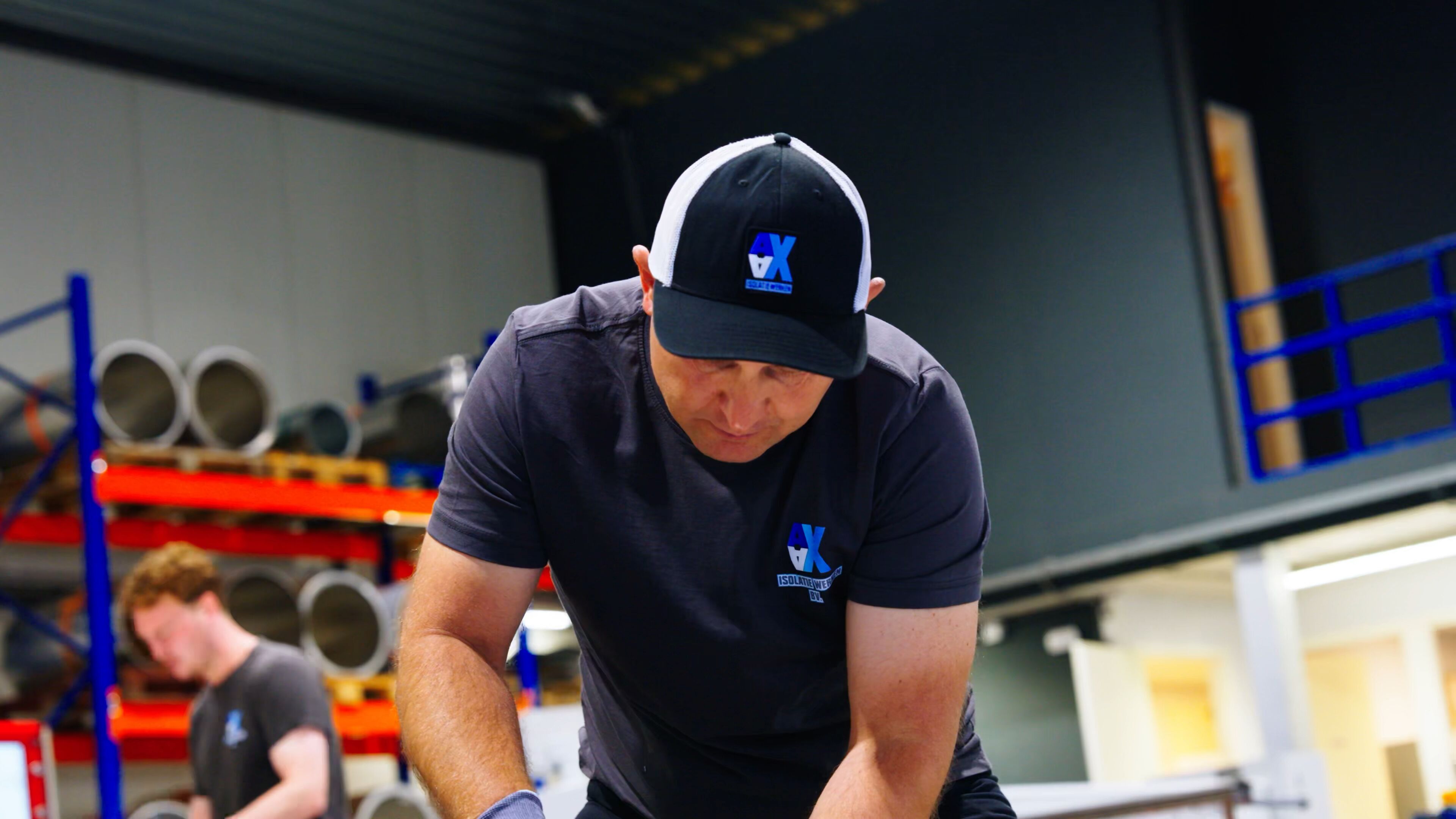 Medewerker van AX Isolatiewerken aan het werk in de werkplaats, met buizen op stellingen op de achtergrond
