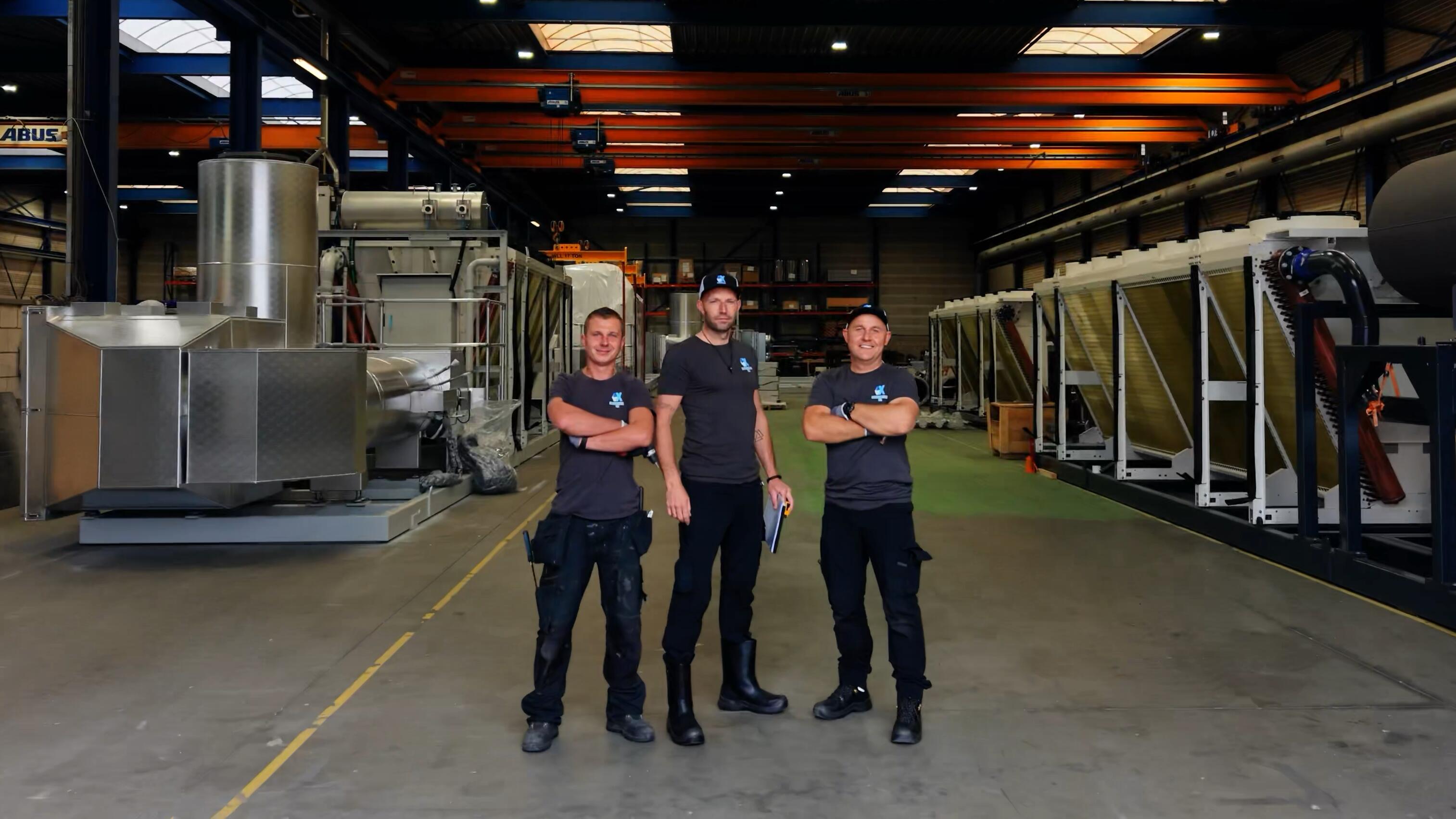 Drie medewerkers van AX Isolatiewerken met de armen over elkaar in een bedrijfshal met geïsoleerde installaties