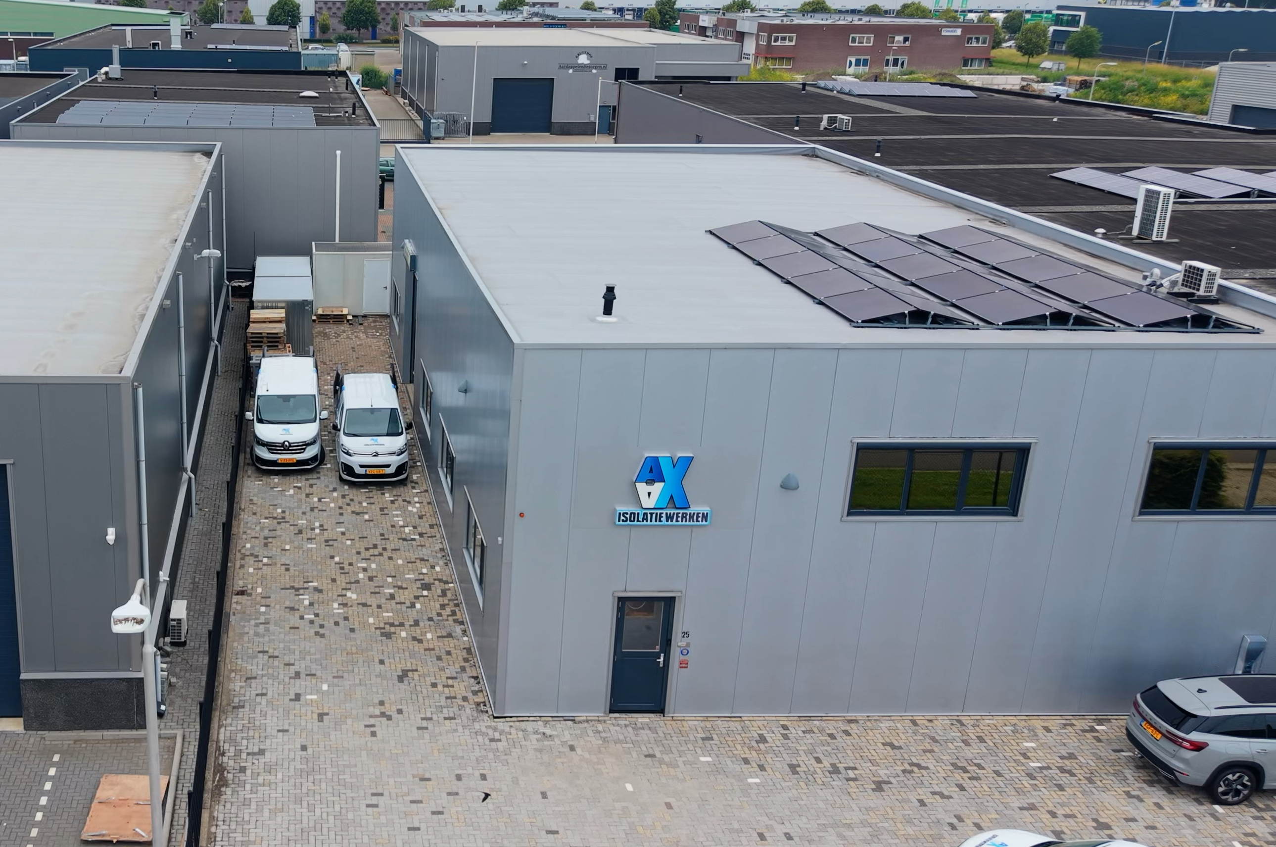 Luchtfoto van een bedrijfsterrein met loodsen en woningen, omringd door weilanden aan het water