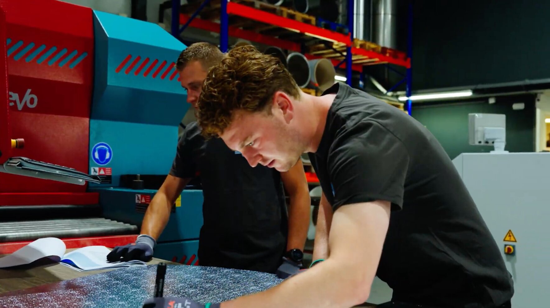 Twee medewerkers van AX Isolatiewerken tekenen plaatwerk af naast een plaatbewerkingsmachine