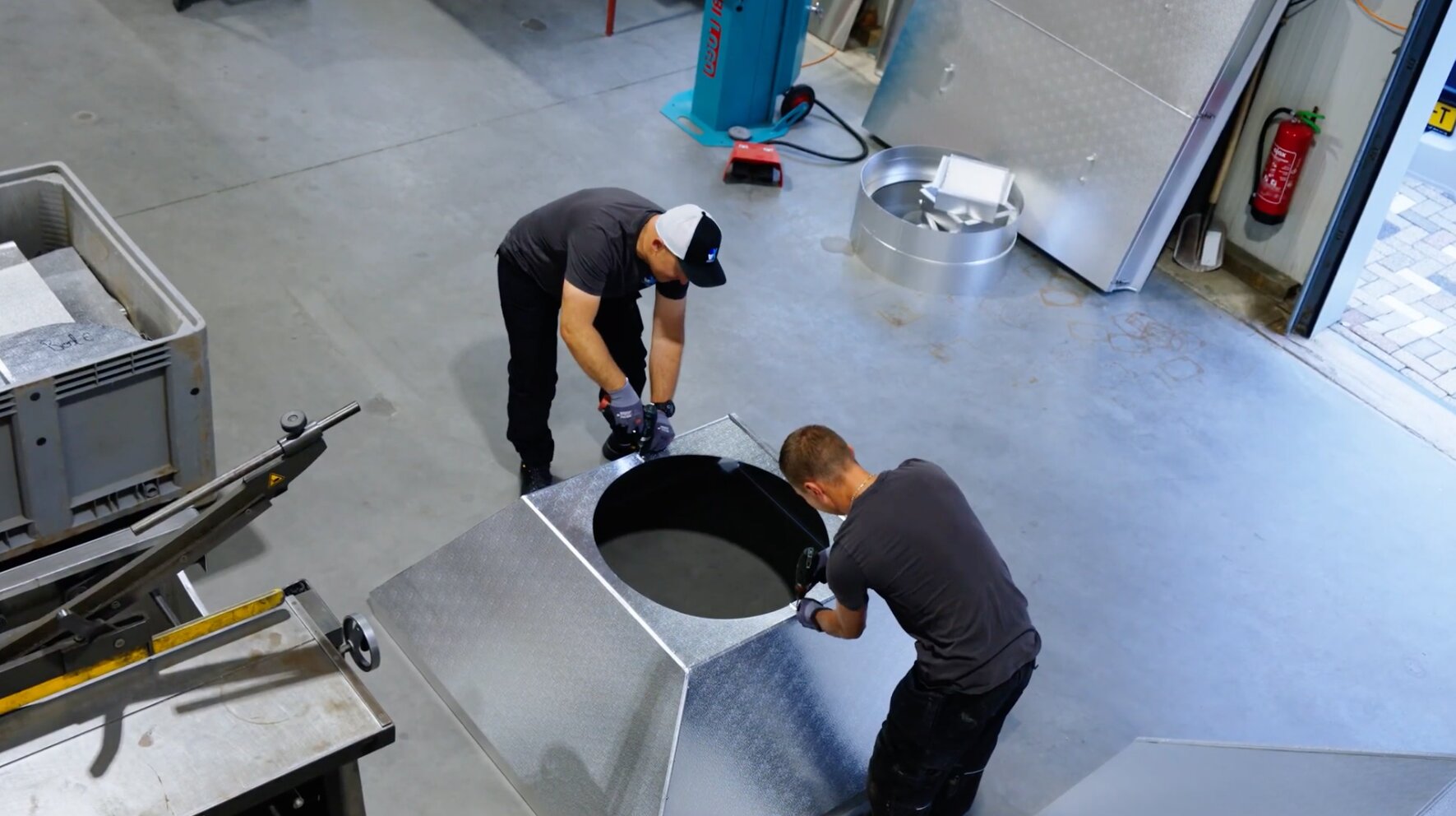 Twee medewerkers van AX Isolatiewerken monteren een plaatwerken ommanteling in de werkplaats